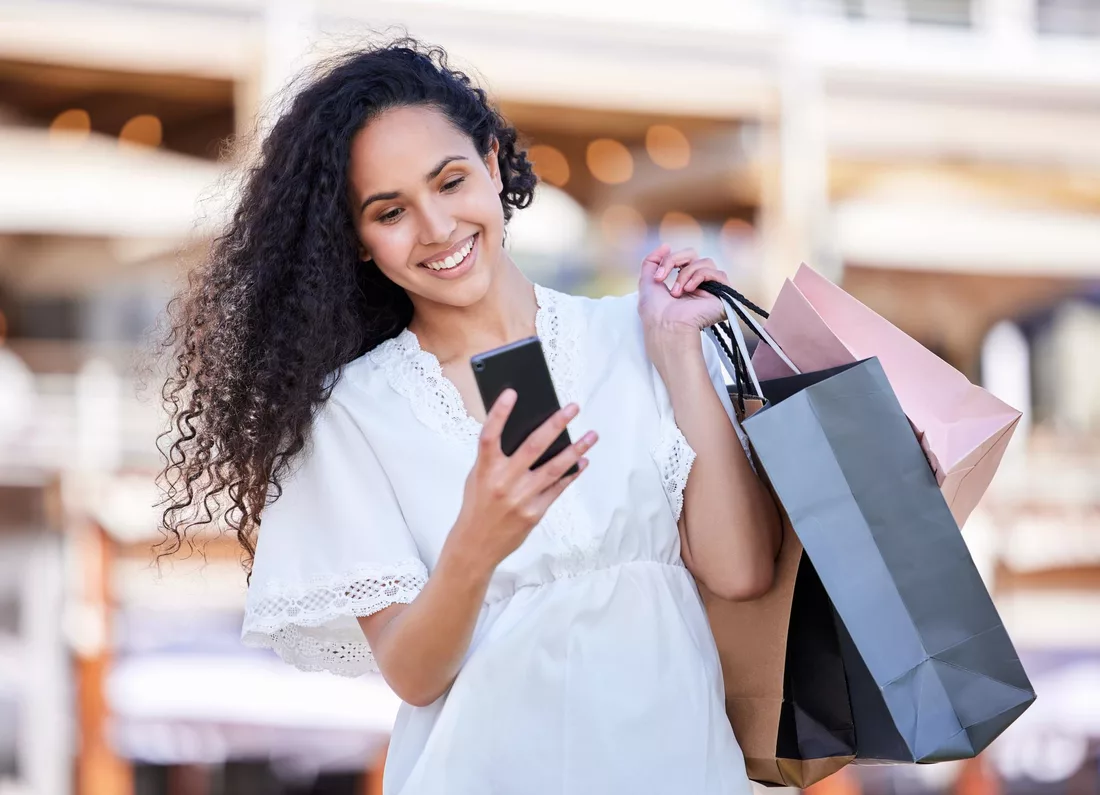 Mulher sorrindo com sacolas de compras olhando o celular